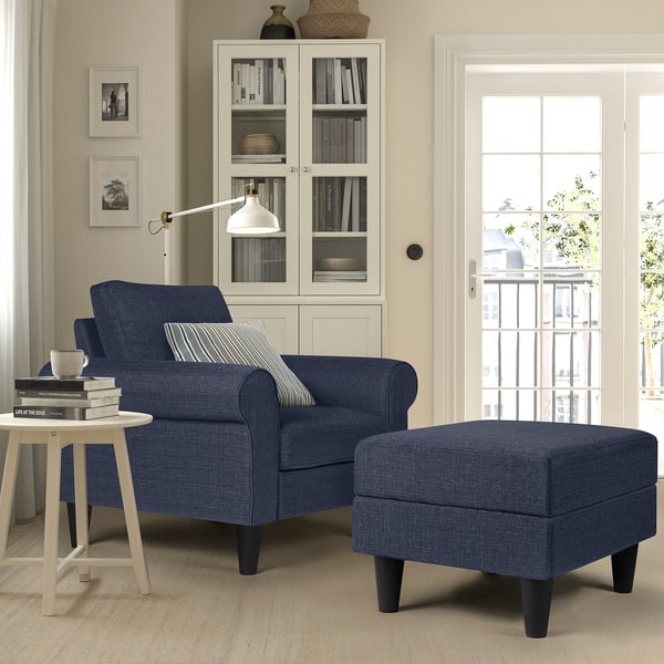 A GAMMALBYN blue armchair and footstool, dark legs, white bookcase, side table with cup and books.
