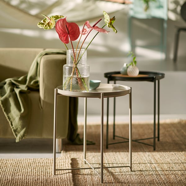 Modern living room with GLADOM side tables, one black, one beige, holding vases with red flowers. Beige table has a removable tray top.