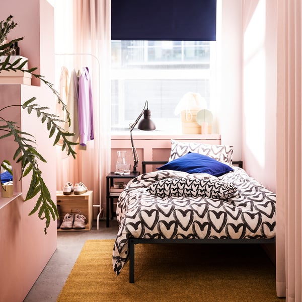 Cosy bedroom with GRIMSBU black metal bed, heart-patterned linens, pink walls, and large window.