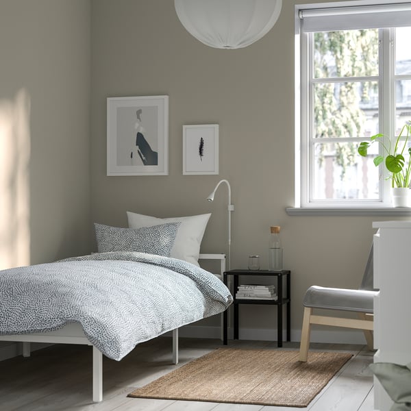 Modern bedroom with white metal bed, low profile for storage, patterned duvet, bedside table with lamp and books, minimalist decor, cosy rug.