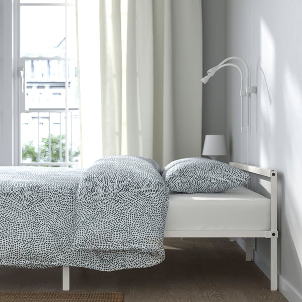 Modern low bed with patterned grey comforter by window, featuring sturdy steel frame and slatted base for air circulation.