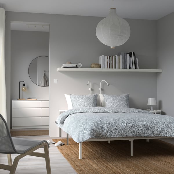 Minimalist bedroom with white GRIMSBU bed, patterned linens, floating shelf lamp, black chair.