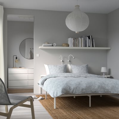 Minimalist bedroom with white GRIMSBU bed, patterned linens, floating shelf lamp, black chair.