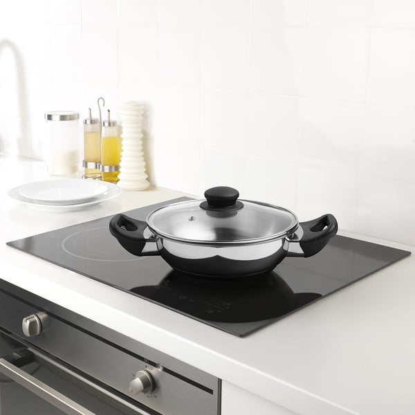 Modern kitchen with stainless steel induction hob, featuring a wok with lid, plates, and oil bottles.