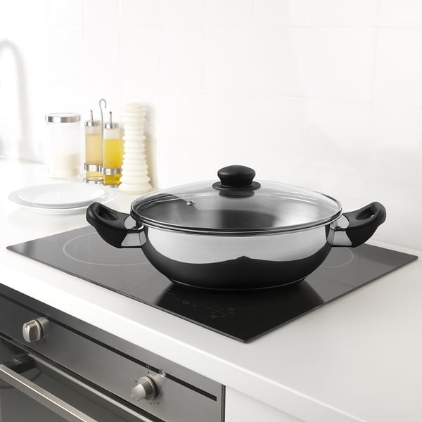 A modern kitchen with a stainless steel wok on an induction hob, featuring a glass lid and two black handles, ready for cooking.