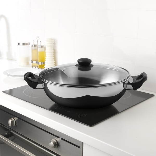 Stainless steel wok with glass lid on induction hob.