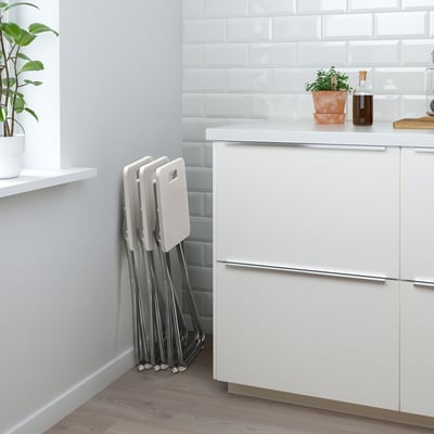 Modern kitchen with white cabinets, foldable GUNDE chairs, houseplants, and minimalist design.