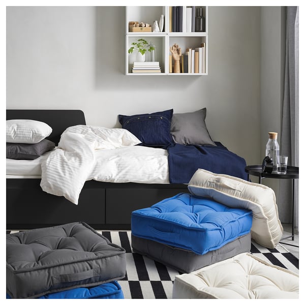 Modern bedroom with black bed, white and navy linens, grey floor cushions, and a blue and grey tufted cushion.
