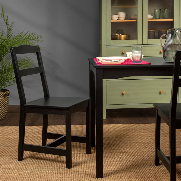 Two black HÄGERNÄS chairs near a dining table with green drawer and cups. A plant on the left.