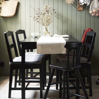 HÄGERNÄS black dining set with floral centrepiece on table, four matching chairs, green vertical wall panel.