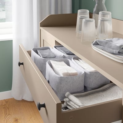 A beige HAUGA sideboard with open drawers containing neatly folded linens. Clear glasses and napkins are on top.