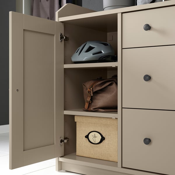 A beige HAUGA storage unit with an open door, revealing shelves holding a helmet, bag, and box.