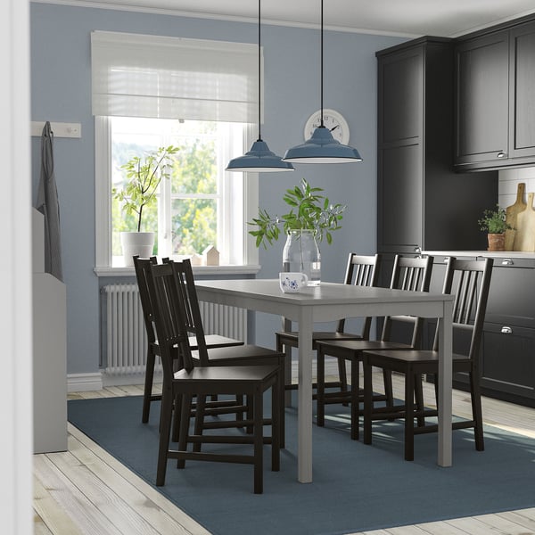 Modern kitchen with grey HAUGA table, six black chairs, two pendant lamps, and blue rug. Central table, large window, blue walls.