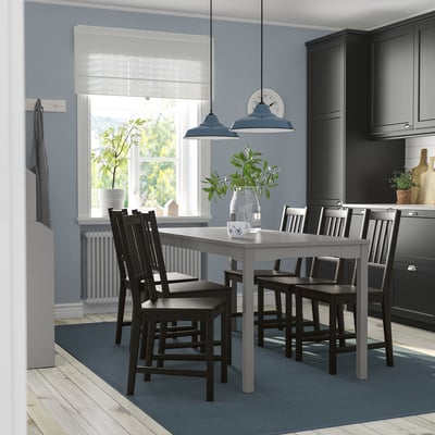Modern kitchen with grey HAUGA table, six black chairs, two pendant lamps, and blue rug. Central table, large window, blue walls.
