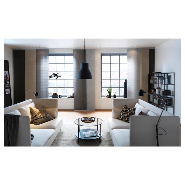 Modern living room with white sofas, glass table, black pendant lamp, large windows, wooden blinds, black floor lamps, rug, bookshelf, and blanket.