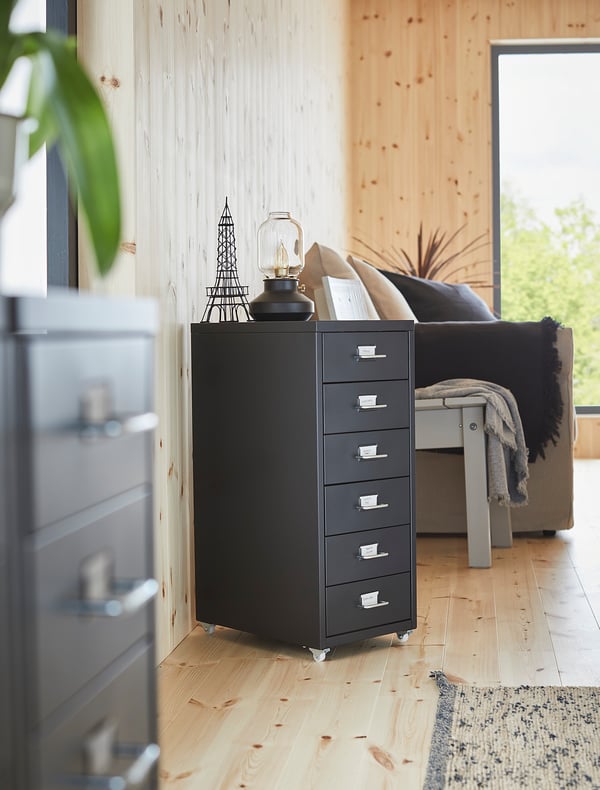 Black HELMER filing cabinet on wheels, modern wooden room, decors on top.
