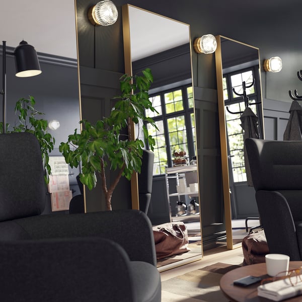 Gold-framed HOVET mirror leaning on wall, reflecting room, surrounded by dark chairs.