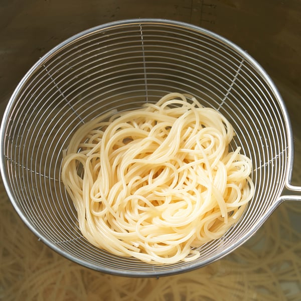 Metal colander filled with cooked noodles, showing its draining function. Handle on side for easy use.