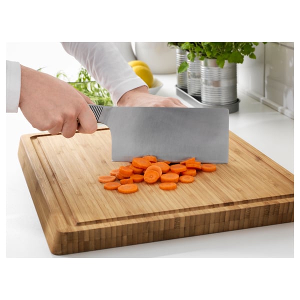 Person is slicing carrots on a wooden cutting board with a stainless steel knife.
