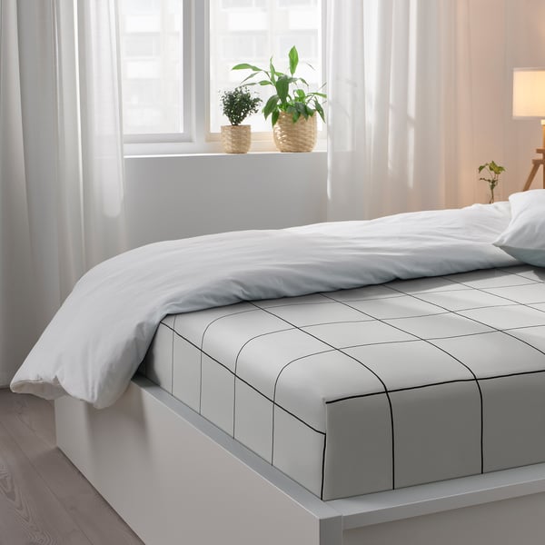 Bedroom with white bed, grey sheet with black chequered pattern. Two plants on windowsill. Soft, pure cotton bedding.