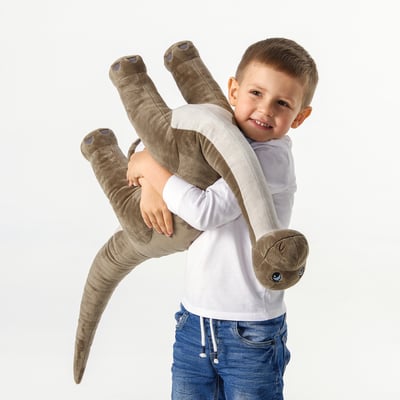 Young boy holding a large soft dinosaur toy. The toy has a long neck and small head, designed for cuddling and play.
