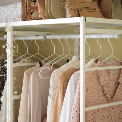White JONAXEL hanging storage with pastel blouses, featuring sleek metal frame and hangers displaying soft neutral tones.