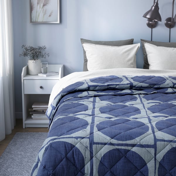 Bed with blue comforter and white pillows on grey walls. Bedside table with books and vase.