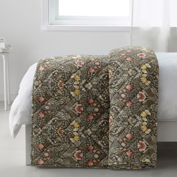 A bed with a KÄRRDUNÖRT flower-patterned comforter in earthy tones, providing warmth and comfort.