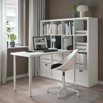 A minimalist home office featuring a white KALLAX shelf with books, a sleek desk, and a bright window.