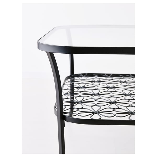 Glass-top table with metal frame, intricate designs, and patterned shelf for storage.