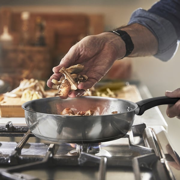 Person adds mushrooms to stainless steel frying pan on stove.