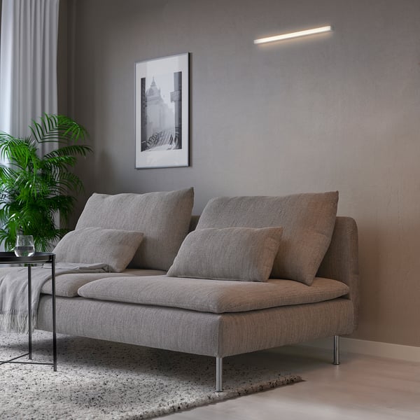 Modern living room with grey sofa, pillows, rug, plant, and wall art. Above the sofa, a KNOPPSLINGA led light illuminates warmly.