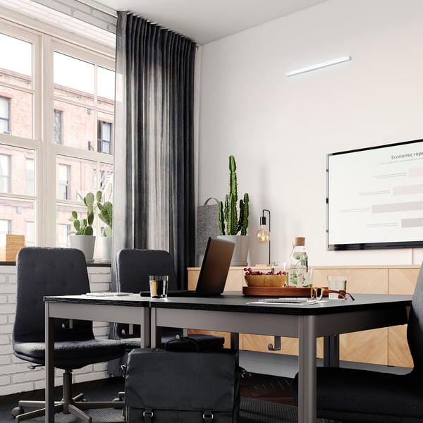 Modern office with desks, laptops, plants, and tv showing an economic report.