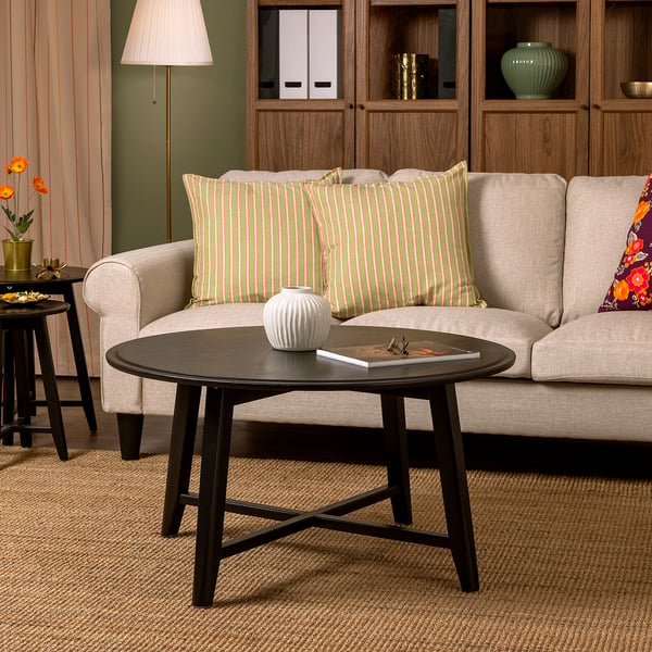 KRAGSTA coffee table: sleek black, round mango wood design, fits cosy living space, small vase and book on top, positioned near beige sofa.