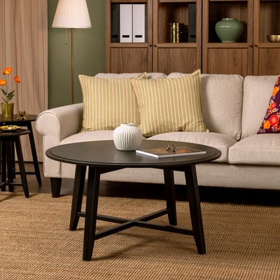 KRAGSTA coffee table: sleek black, round mango wood design, fits cosy living space, small vase and book on top, positioned near beige sofa.