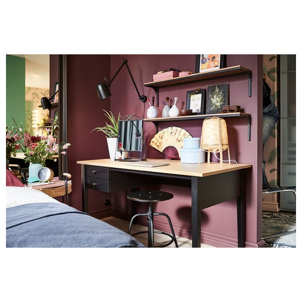 Cosy home office space with dark red walls, wooden desk, and stool. Decorated with plants, books, and decorative items.
