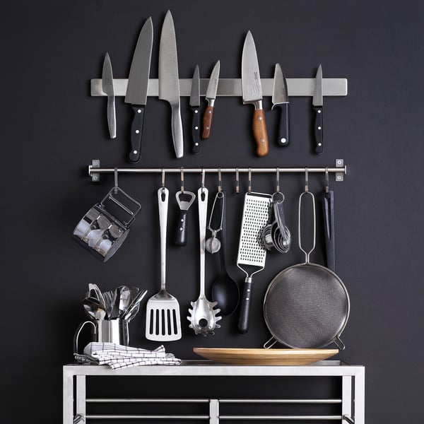 Wall-mounted kitchen storage with knives, utensils, and accessories neatly organised on a dark background.