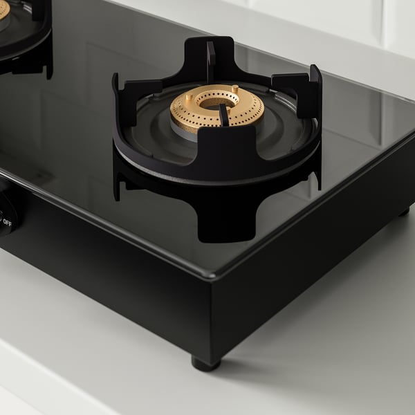 Black gas stove burner with cast iron supports on a glass cooktop.