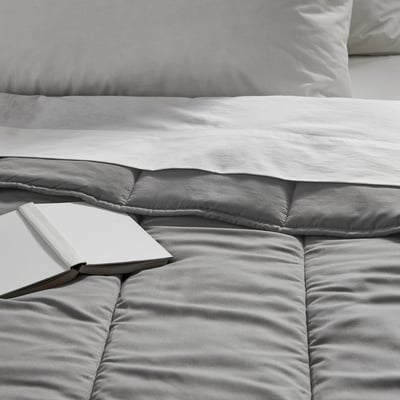Soft, grey comforter with smooth texture, neatly made bed with open book; displays quality & comfort.