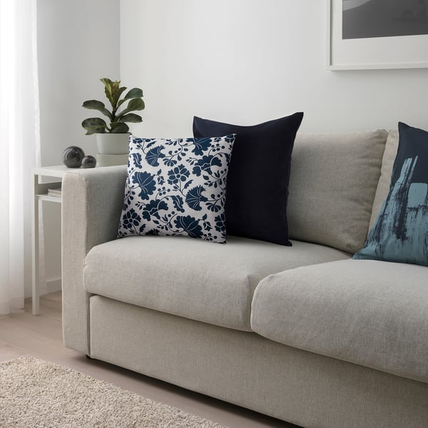 A grey sofa with cushions in floral, navy, and blue patterns adds decorative and comfortable touch; small plant and side table nearby.