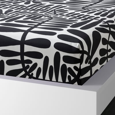 Black and white leaf-patterned bedsheet on white bed, showcasing its nature-inspired design and moisture-absorbing cotton/viscose blend.