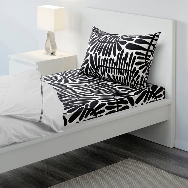 White bed with large black leafy pattern, neat, minimalist room with bedside table and lamp.