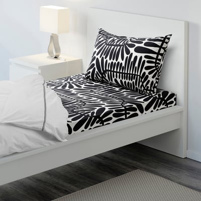 White bed with large black leafy pattern, neat, minimalist room with bedside table and lamp.