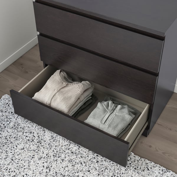 Open dresser with folded clothes; smooth, dark wood drawers, light rug.