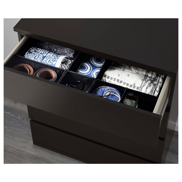 Black chest of drawers with open drawer, showing neat stacks of colourful clothes and accessories in compartments.