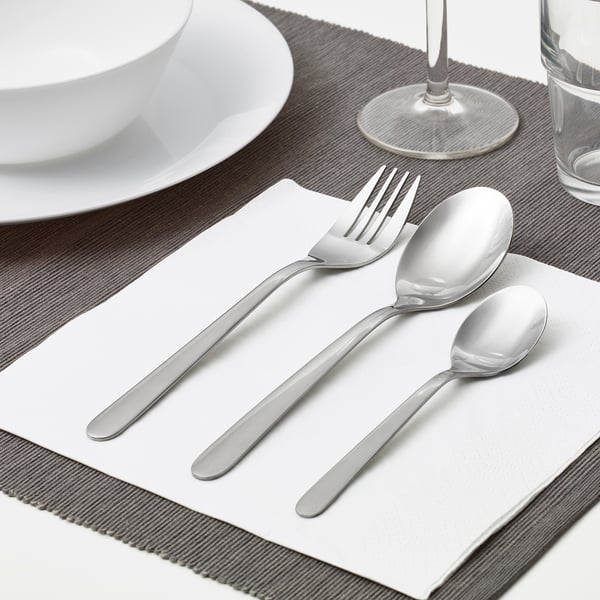 A neatly arranged table setting featuring a fork, spoon, and teaspoon on a napkin, alongside a plate and glass, showcasing everyday cutlery.