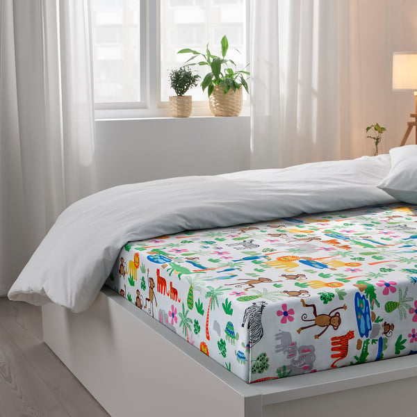 Bright bedroom with jungle-themed bed, white pillows, cosy blanket, and potted plants. Soft light, inviting.
