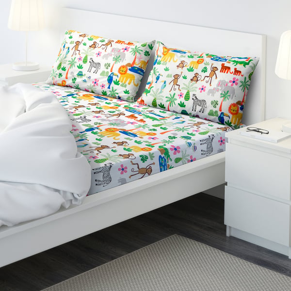 Childs bed with white NATTHÄGER sheet set featuring colourful jungle animals, smaller than nearby drawers.
