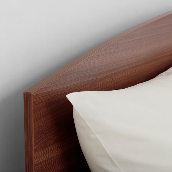 Clean, modern bed frame with sleek, dark wood finish leaning against a light blue wall. A white pillow rests on it for comfort.