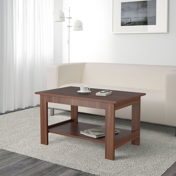 Wooden coffee table with two shelves. Top shelf holds a cup and remote. Bottom shelf holds magazines.